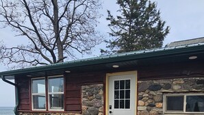 Une maison en pierre avec un revêtement extérieur en bois, une porte blanche et un petit porche.