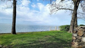 Une zone herbeuse, bordée d’un mur de pierre et agrémentée d’arbres, qui offre une vue sur une étendue d’eau.