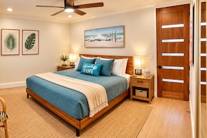 Un dormitorio con cama, mesitas de noche, ventilador de techo, puerta de madera y decoración en la pared.