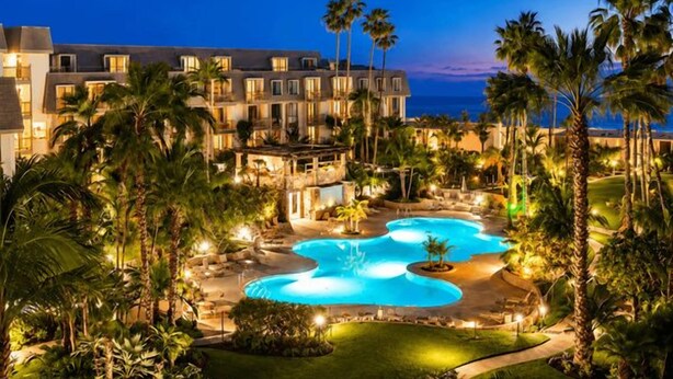 A resort with a large pool, palm trees, and a building with multiple windows. - Garden-View Condo at North Coast Village | G5 (Oceanside)
