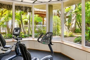 Un gimnasio interior con bicicletas estáticas y vistas a un jardín tropical.