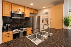 A modern kitchen with granite countertops, stainless steel appliances, wooden cabinets, and a built-in sink. - Garden Cottage G5 + Patio | North Coast Village (Oceanside)
