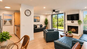 A modern living room with a fireplace, a television, and a view of the outdoors. - Garden-View Condo at North Coast Village | G5 (Oceanside)