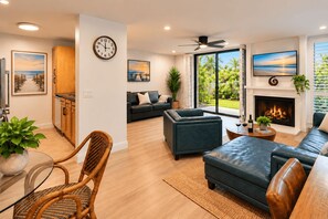 A modern living room with a fireplace, a sofa, a dining area with a table and chairs, and a kitchen in the background. - Garden Cottage G5 + Patio | North Coast Village (Oceanside)
