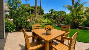 An outdoor wooden table with chairs, a vase of flowers, and a well-maintained garden with various plants and a lawn. - Garden-View Condo at North Coast Village | G5 (Oceanside)