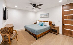 A bedroom with a bed, a chair, a nightstand, a wooden door, and a ceiling fan. - Garden-View Condo at North Coast Village | G5 (Oceanside)