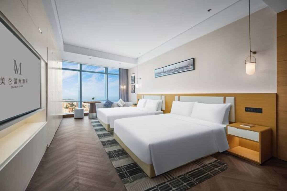 A modern hotel room with two beds, a large window, a small table, and a nightstand.