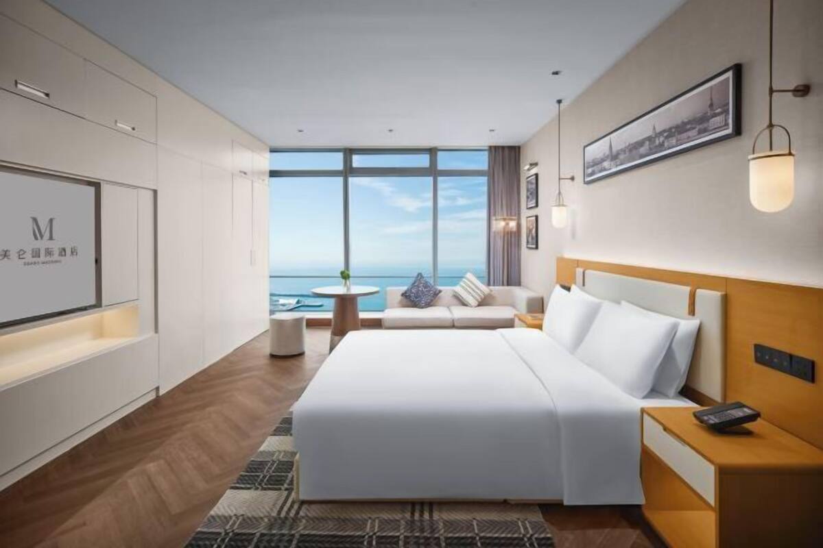 A hotel room with a large bed, a sofa, a small table, and a view of the sea.