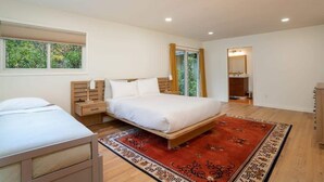 Une chambre à coucher avec un grand lit, un lit plus petit, une table de chevet, une commode, un miroir et une fenêtre avec des stores.