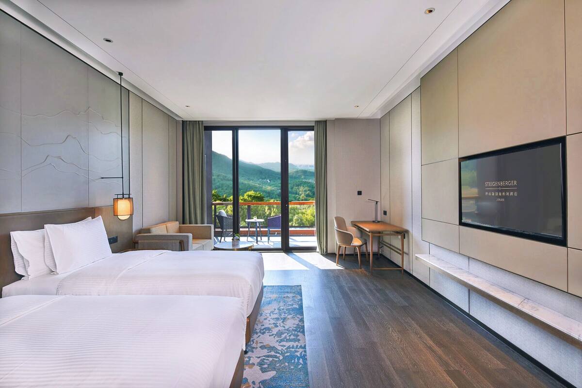 A hotel room with a large bed, a desk, a chair, and a TV on the wall.