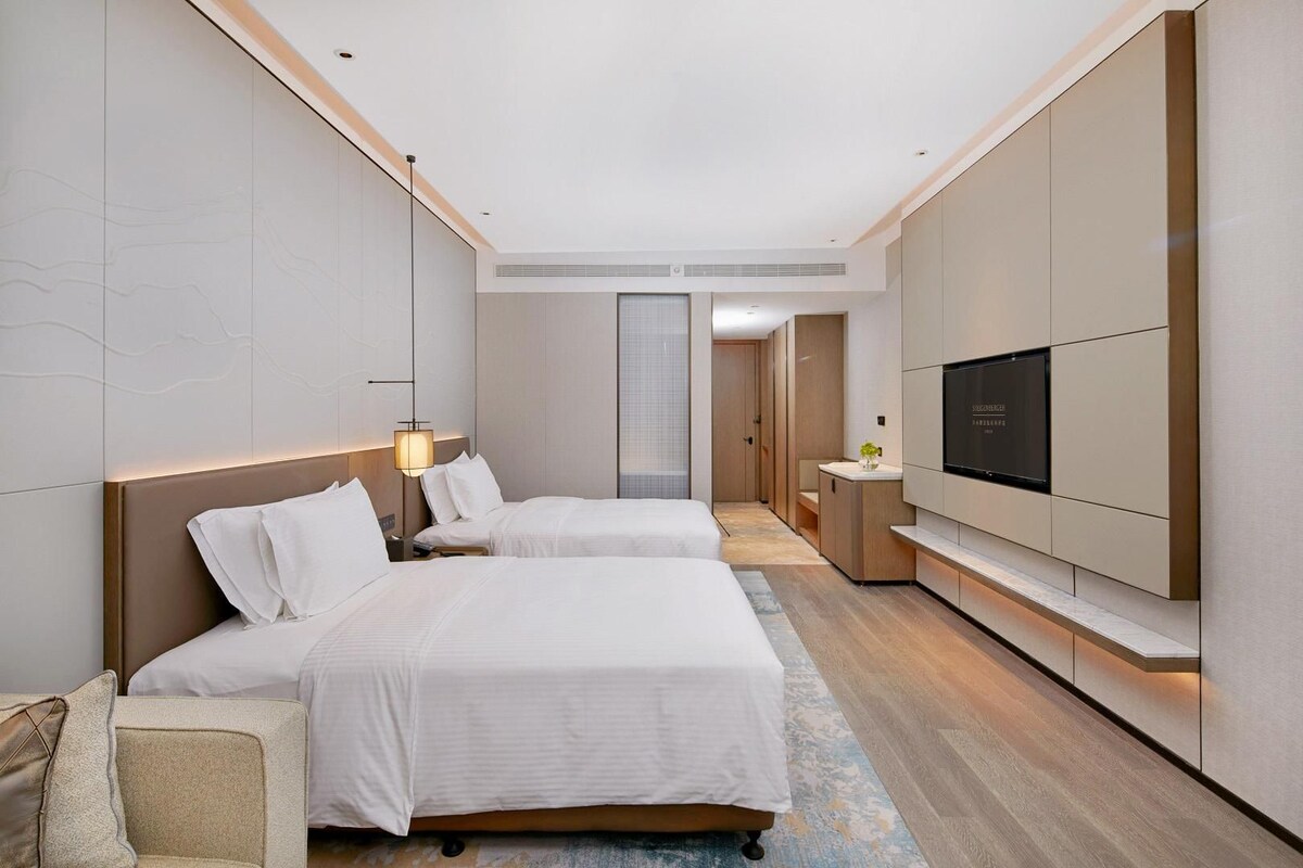 Ein modernes Hotelzimmer mit zwei Betten, einem Flachbildfernseher und einem begehbaren Kleiderschrank.
