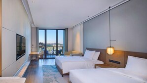Une chambre d’hôtel moderne avec deux lits, un bureau et un balcon offrant une vue agréable.
