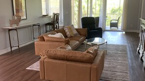 En rummelig stue med en stor L-formet sofa, et spiseområde med bord og stole, og en balkon med udsigt.