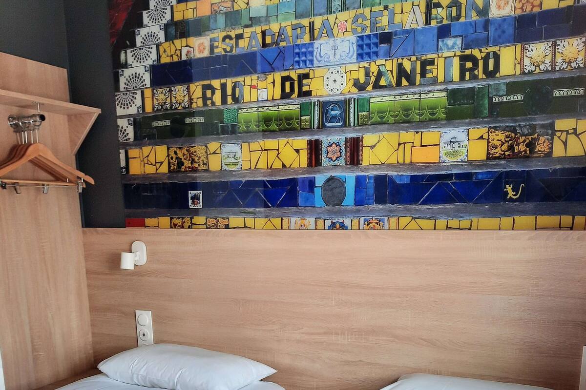 A hotel room with two beds, a wooden headboard, and a colorful mosaic wall.