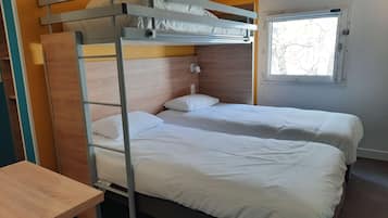 A bunk bed with two beds, a wooden desk, and a window with a view of trees.