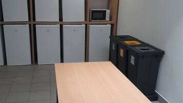 Una habitación con una larga mesa de madera, seis armarios blancos, un microondas y un cubo de basura.