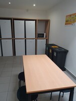 Una habitación con una larga mesa de madera, seis armarios blancos, un microondas y un cubo de basura.