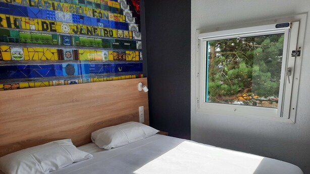 Een slaapkamer met een houten hoofdeinde, wit beddengoed en een raam met uitzicht op groen.