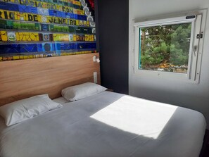 Un dormitorio con cabecera de madera, ropa de cama blanca y una ventana con vistas a la vegetación.