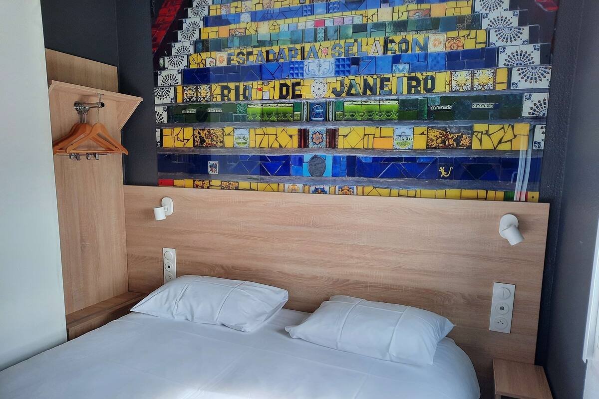 A hotel room with a wooden headboard, a bed with white linens, and a colorful mosaic wall.