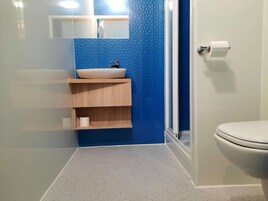 Un baño con un inodoro blanco, una pared azul con textura, un lavamanos blanco con repisa de madera y un espejo sobre el lavamanos.