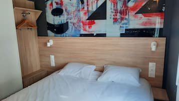 A hotel room with a wooden headboard, a bed with white linens, a wooden wardrobe, and a large abstract painting above the bed.