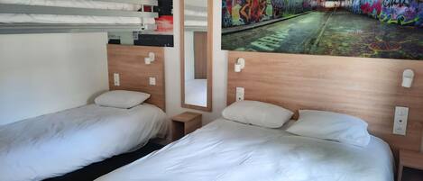 Habitación de hotel con dos camas individuales, cabecero de madera, mesita de noche pequeña, un espejo y un mural en la pared que muestra un túnel cubierto de grafitis.