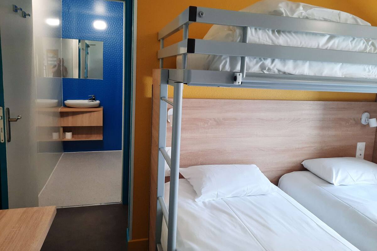 A bunk bed with white bedding and pillows, a wooden headboard, and a small bedside table.