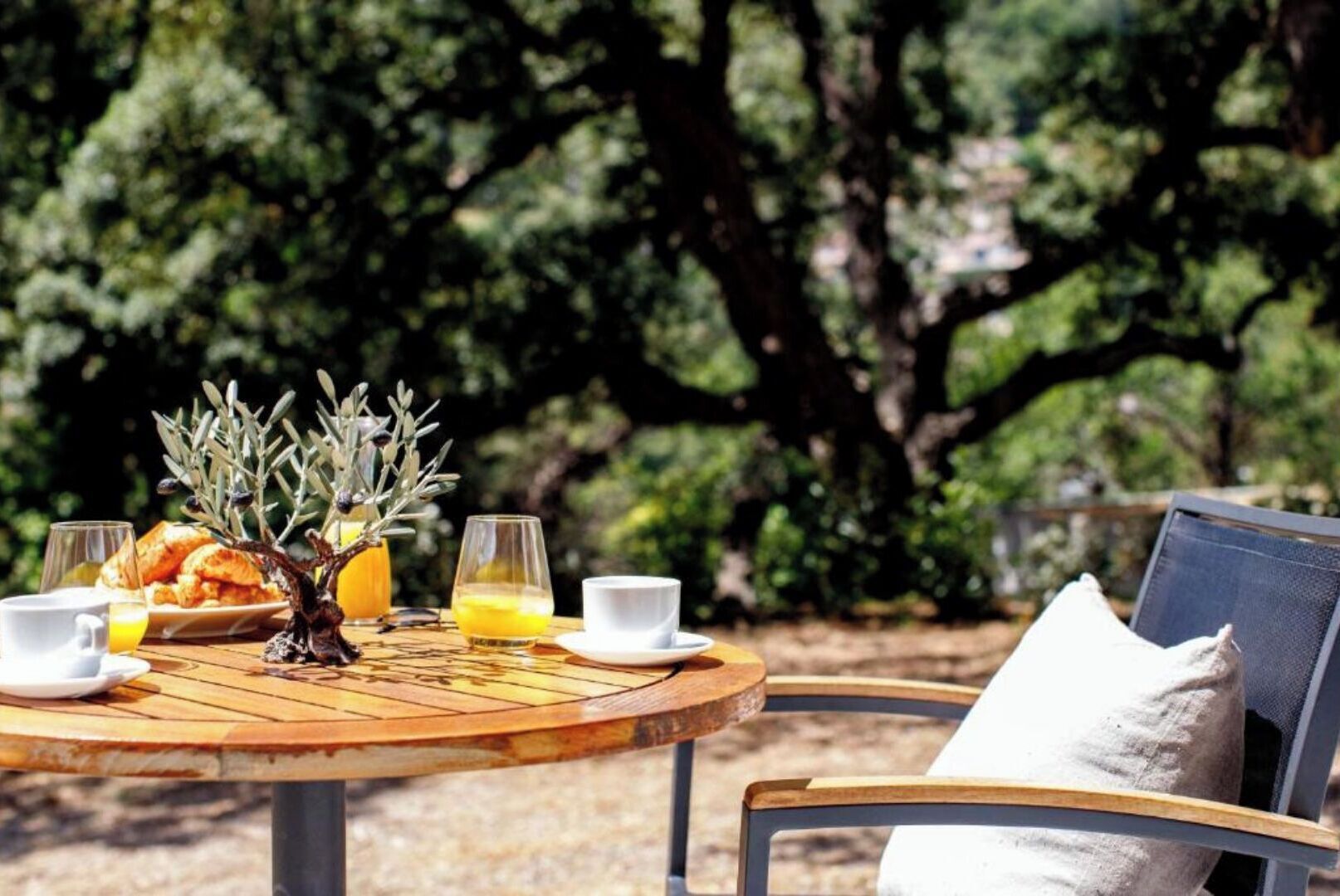 A round wooden table with breakfast items, two glasses of orange juice, and a small vase with dried branches.