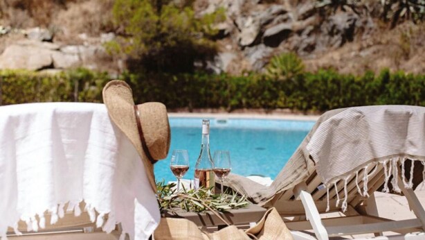 A poolside setting with lounge chairs and a table, a bottle, and glasses of wine.