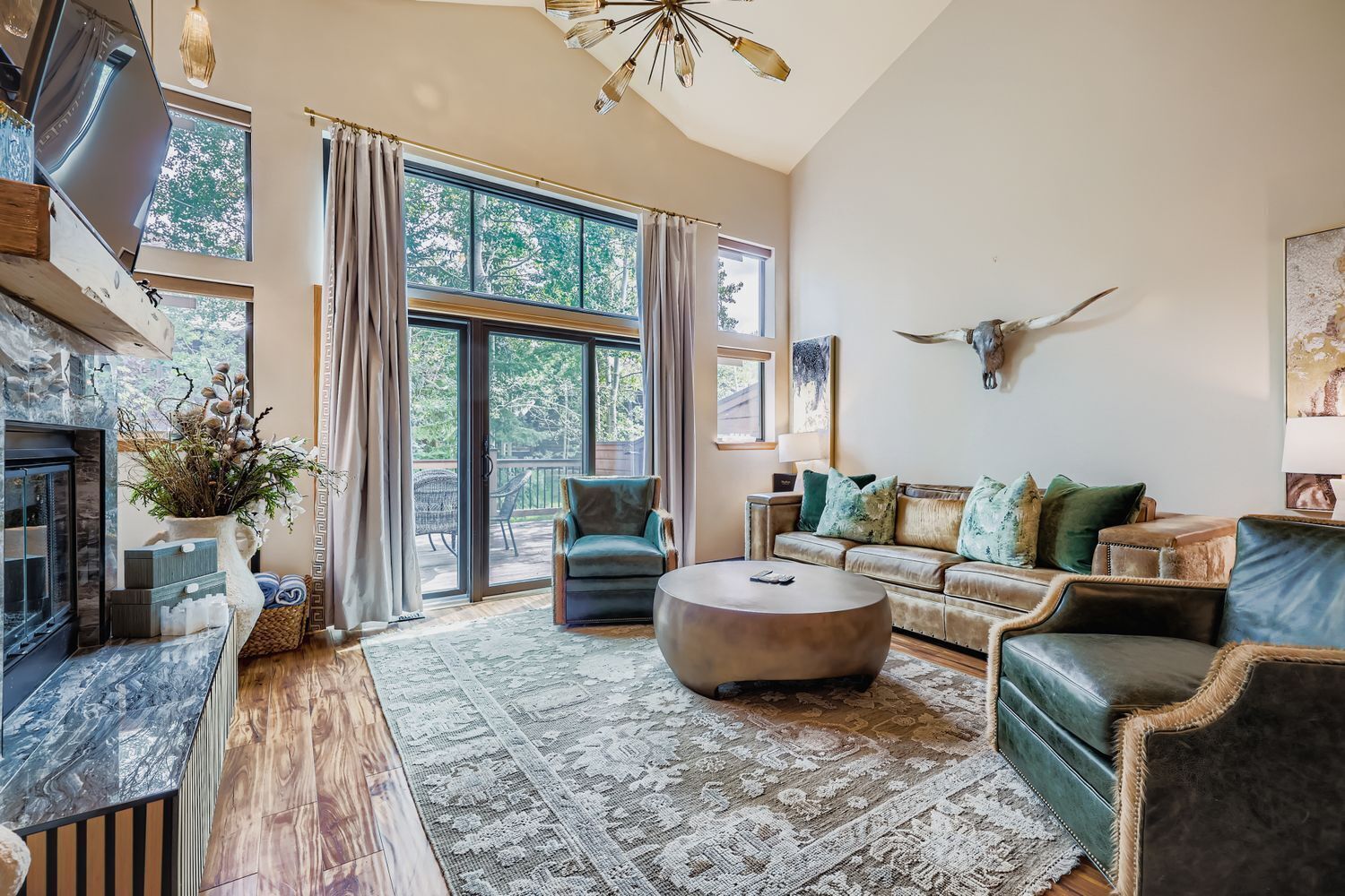 A spacious living room with a fireplace, large windows, a sofa set, and a mounted animal head on the wall.