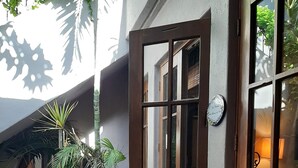 A courtyard with a wooden bench, potted plants, and a stone pathway leading to a wooden door with glass panels.