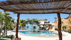 A pool area with a wooden pergola, lounge chairs, and palm trees.