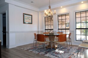A dining area with a chandelier, a table with chairs, and large windows with a view of the outside.