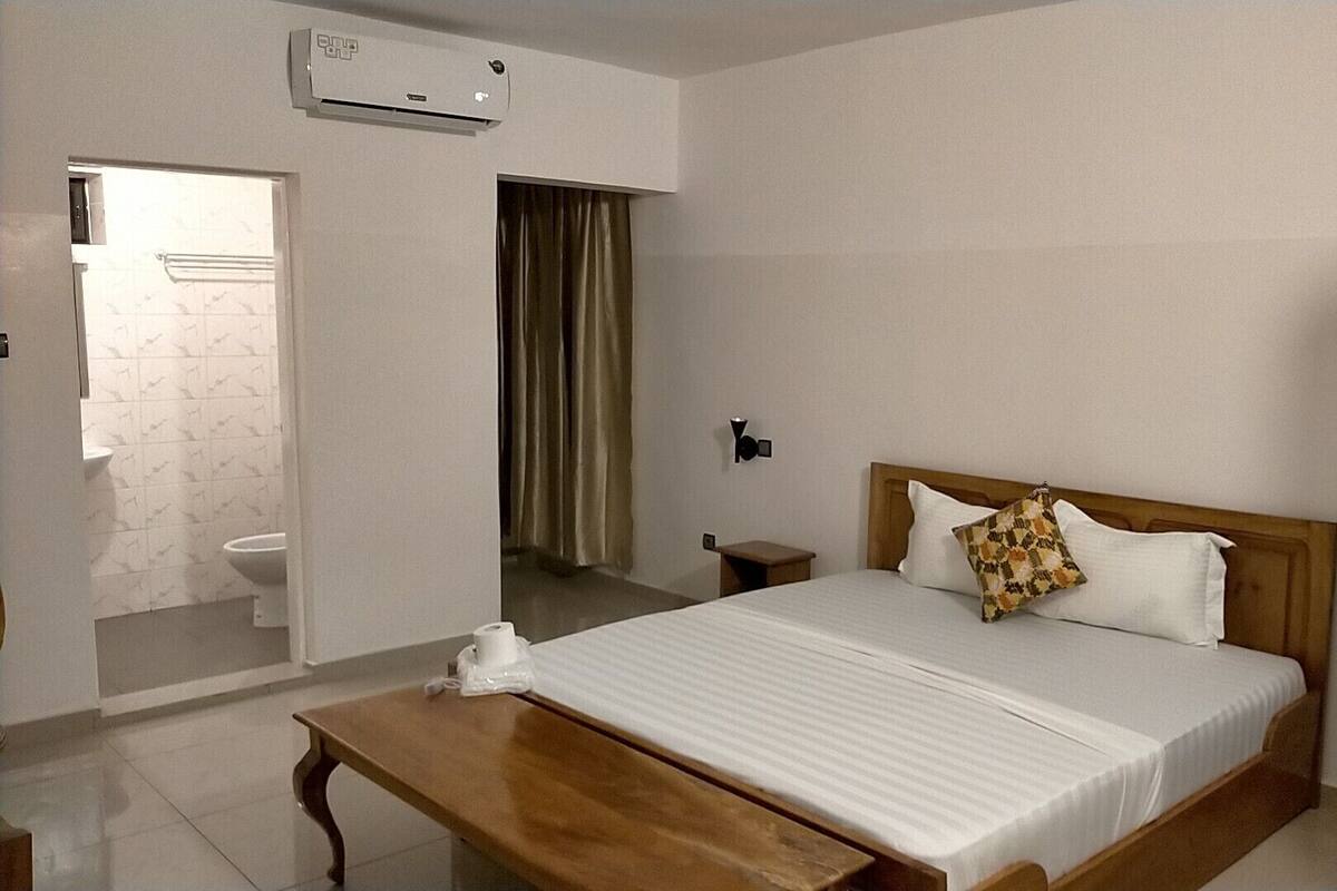 Habitación de hotel con cama, mesita de noche y baño visible a través de una puerta abierta.