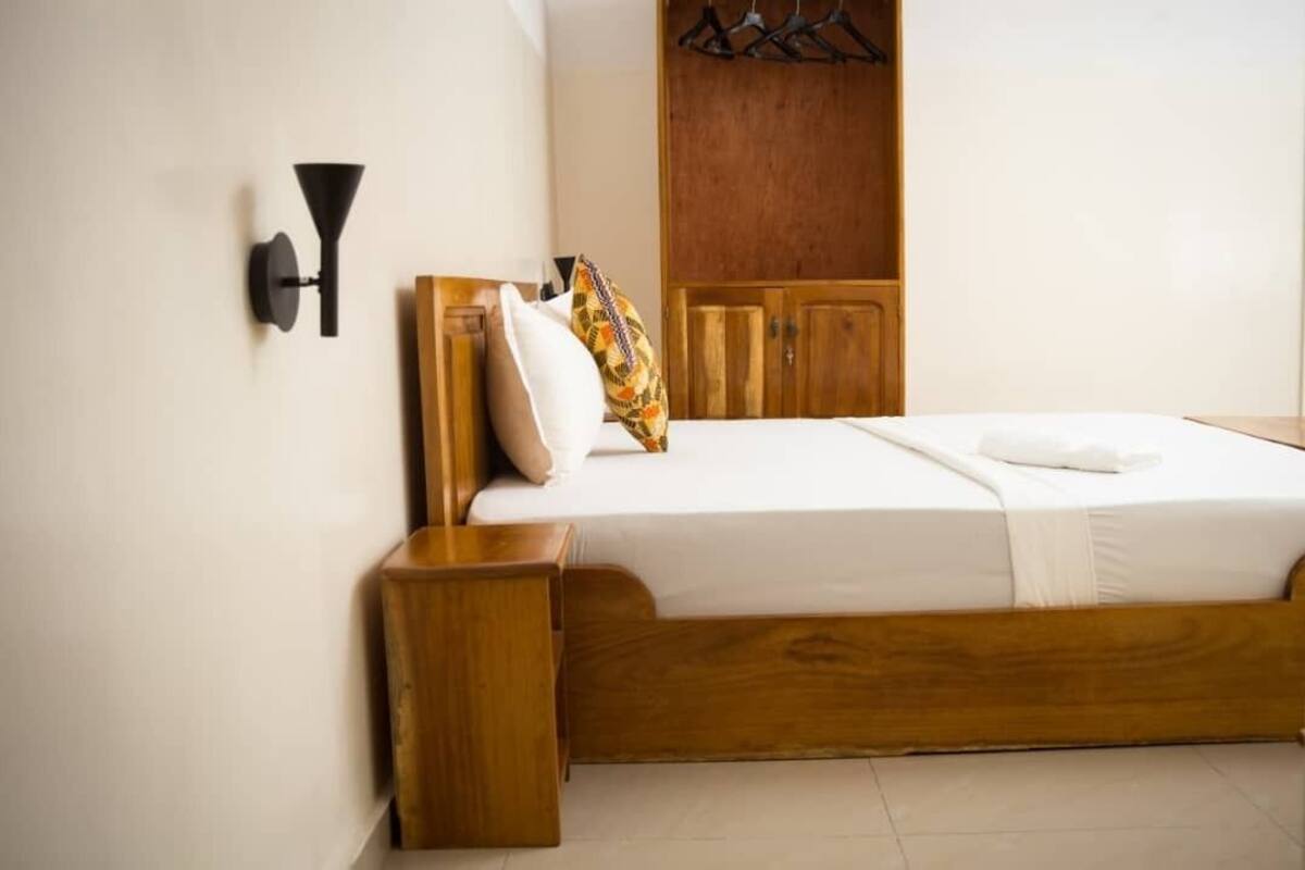 Un dormitorio con una cama de madera, una mesita de noche, un armario y una lámpara fijada a la pared.
