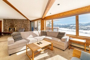 A spacious living room with a large sectional sofa, a wooden coffee table, and a stone wall. - Covered Parking, Cozy, spacious with beautiful views on the bus line (Fraser)
