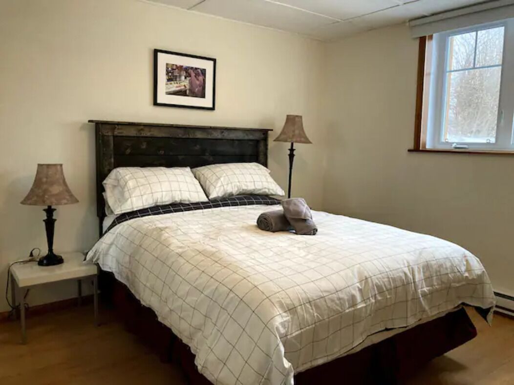 Een slaapkamer met een bed, twee bedlampen, een ingelijste foto aan de muur en een raam.