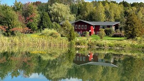 Una casa rossa con uno stagno di fronte, circondata da alberi e un cielo sereno.
