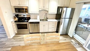A modern kitchen with white cabinets, stainless steel appliances, and a wooden dining table.