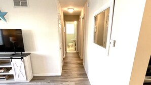 A hallway with a flat-screen TV on a stand, a white console table, and a patterned rug.