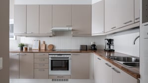 Una cocina moderna con armarios de color claro, encimera de madera, horno empotrado, cafetera y lavaplatos.