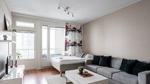 Una sala de estar moderna con un sofá gris, una mesa de centro blanca y una cama con ropa de cama blanca.