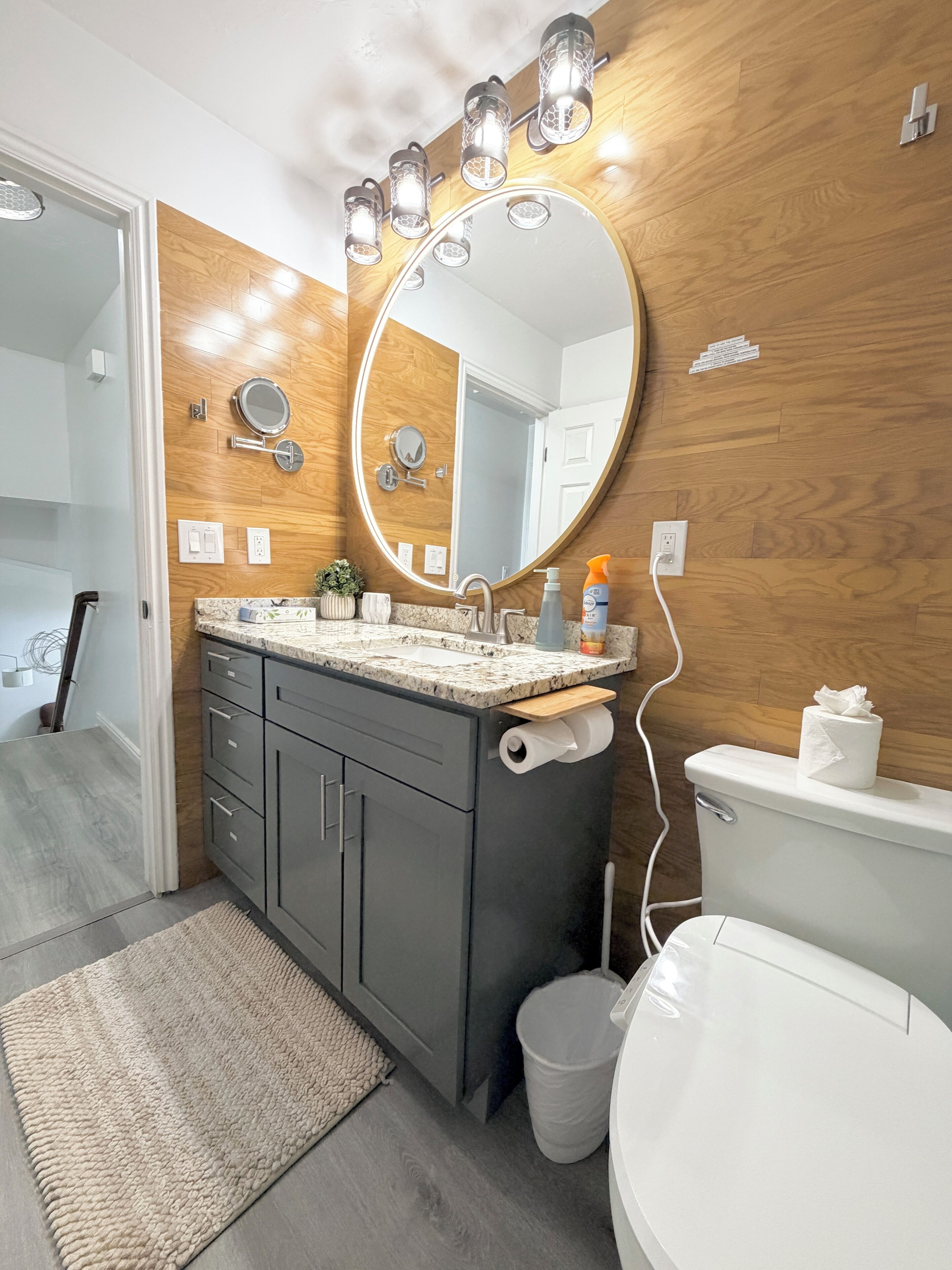 A modern bathroom with a wooden vanity, a round mirror, and a toilet.