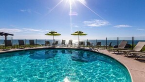 Ein Swimmingpool mit Liegestühlen und Sonnenschirmen, mit Blick auf ein Gewässer.
