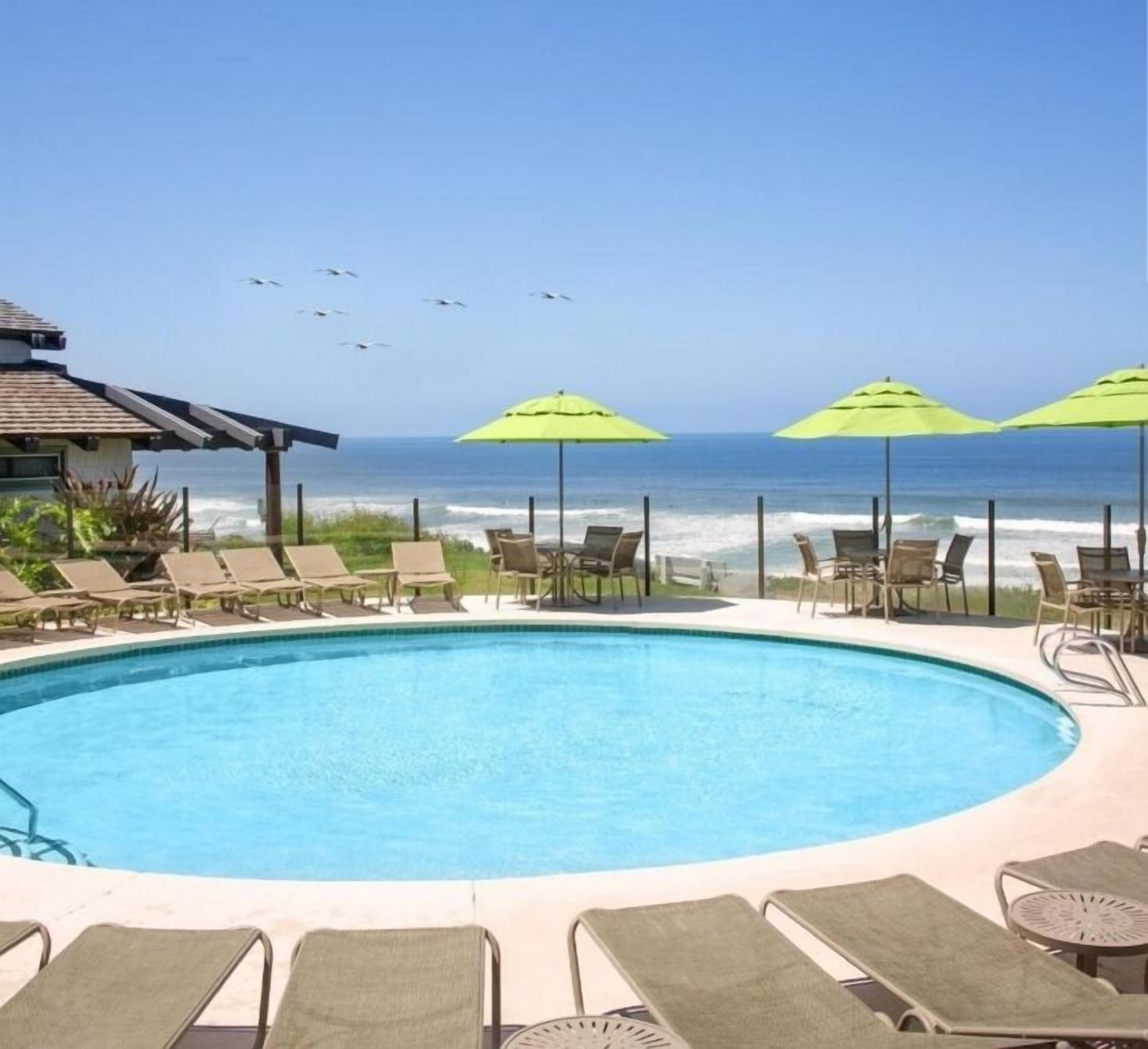 A pool with lounge chairs and umbrellas, overlooking the ocean.
