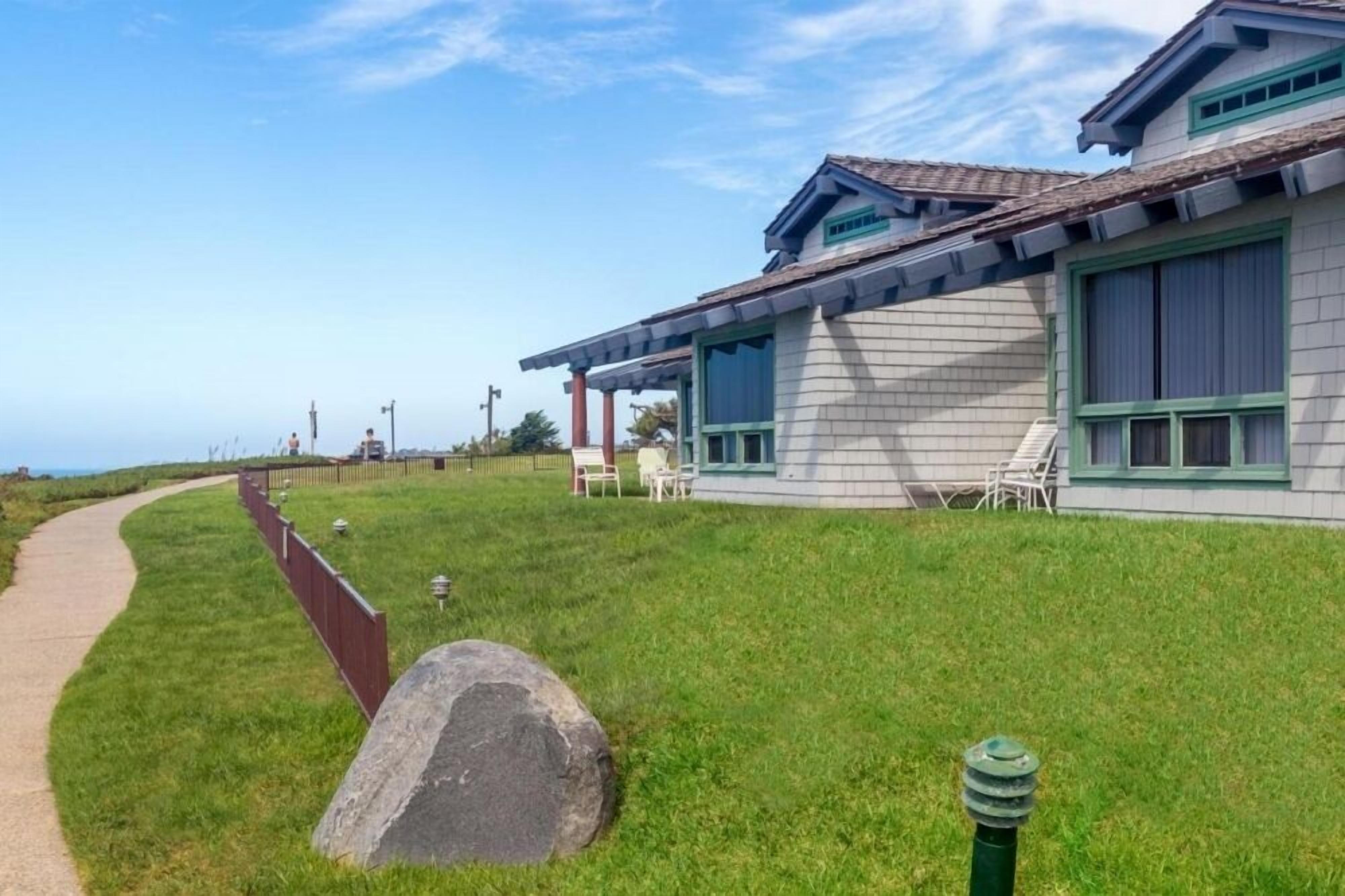 A house with a covered patio, a pathway, and a grassy area.