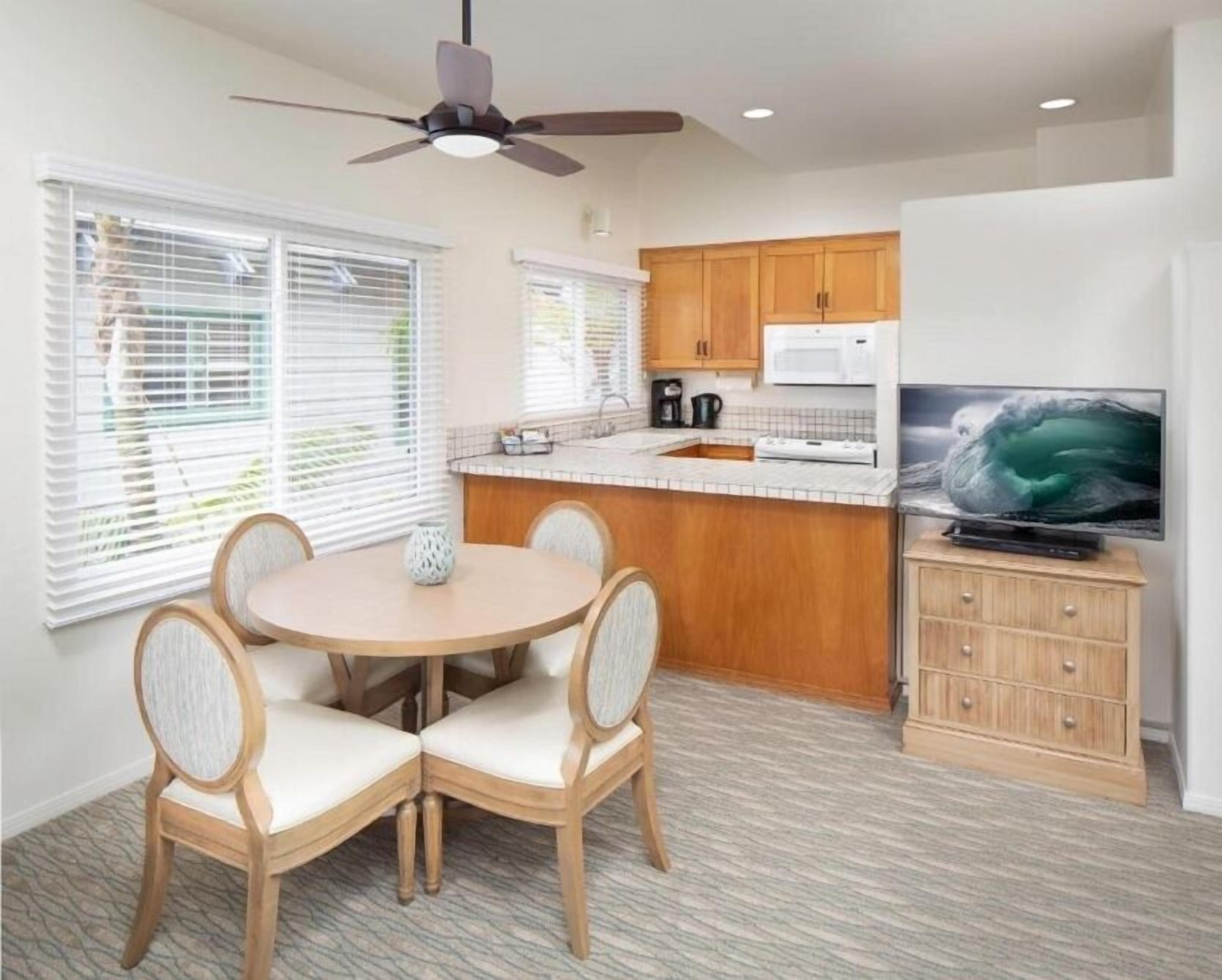 A compact kitchen with a dining area, a ceiling fan, and a television.