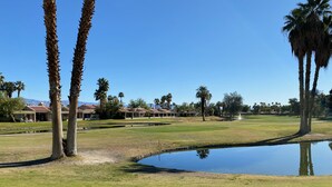Ein Golfplatz mit Teich, Palmen und einem Gebäude mit rotem Dach im Hintergrund.