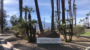 Schild für den Cathedral Canyon Golf & Tennis Club, umgeben von Palmen und einem Bergpanorama.